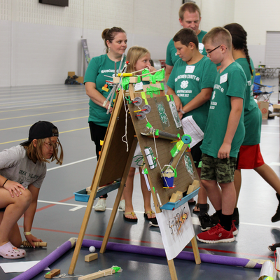 Two adults working with a group of youth on a machine made with everyday objects.