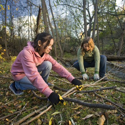 Two girls cleaning up sticks in a wooded area.