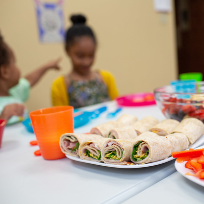 Healthy food on a table with children and caregiver in background. 