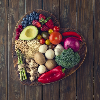 A heart shaped bowl filled with healthy foods like berries, broccoli, grains, tomatoes and asparagus. 