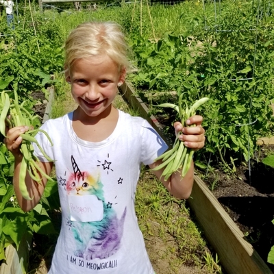 girl holding up beans she picked and smiling in the garden