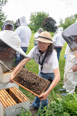 A woman shows a beehive to other beekeepers.