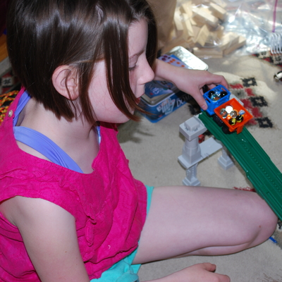 A girl holding toy train cars filled with marbles on a toy track.