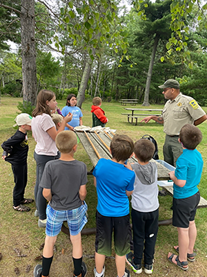 A park ranger talking to a group of kids outdoors.