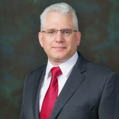 A man with glasses and gray hair wearing a suit with a red tie.