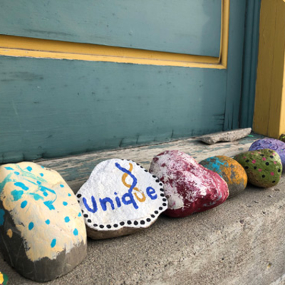 A line of colorful, hand-painted rocks on the sidewalk outside a building.