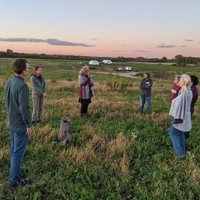Group of adults standing in a field with a beautiful sunset in the background.