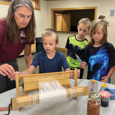 Master Gardener Sally Jacobsen shows a group of children how to use a weaving loom.