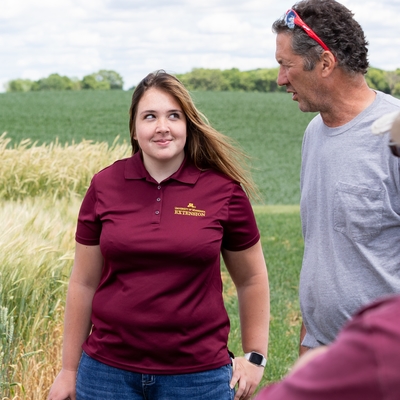 Abby wearing an Extension polo shirt, looks to farmer Ron as he talks. Colleen is on her other side.