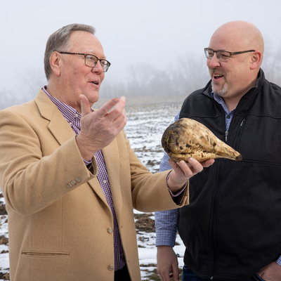 Tom Peters holding a sugarbeet and talking with Eric Watson in a field with snow.