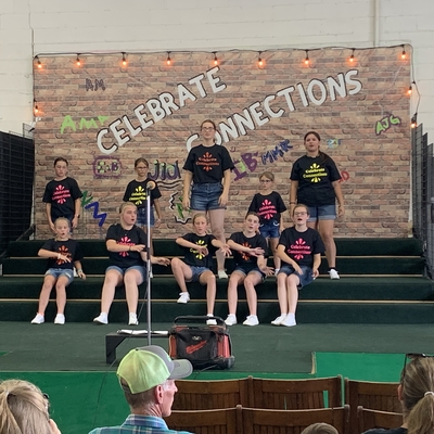 A group of youth wearing black t-shirts performing on a stage with a backdrop containing the words, "Celebrate connections."
