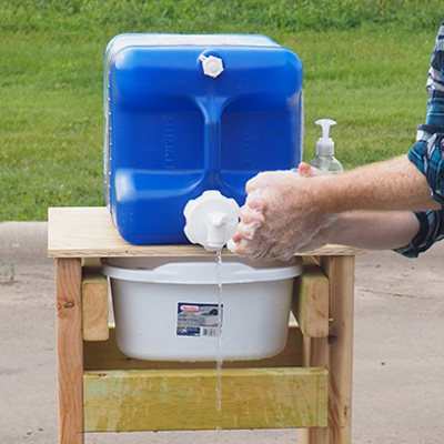 A person washes their hands at a homemade, outdoor handwashing station.