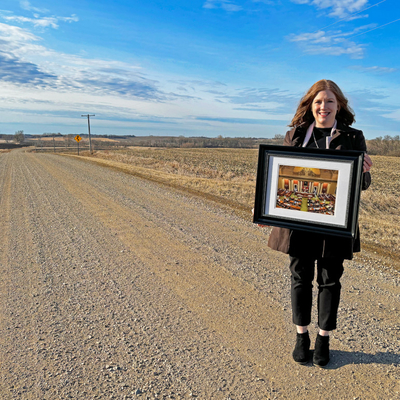 Amy Johnson stands on a gravel road holding a framed photo