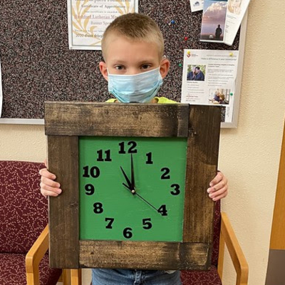 A boy holding a clock with a green face and a thick wood frame