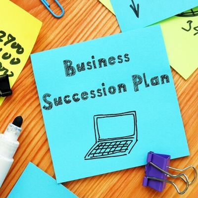 A post-it note with the words business succession planning written on it.