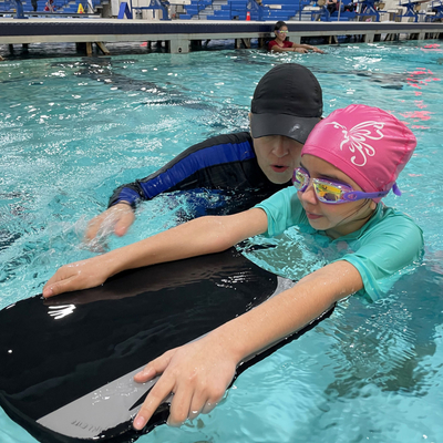 Youth with swimming instructor using a kickboard