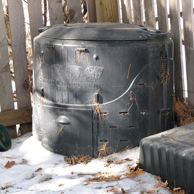 Compost bin by a wooden fence in a yard during winter with snow