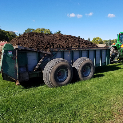 Composted manure being hauled by a tractor on a field.