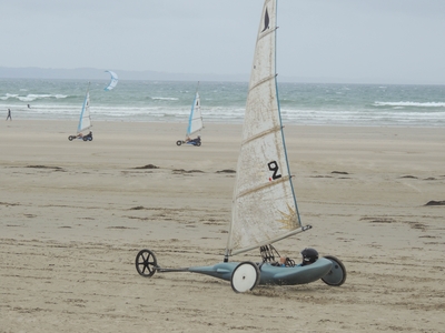 A wind-powered vehicle with a sail on a beach.