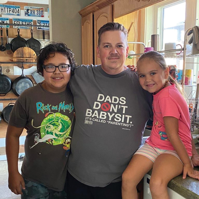 Dad and son and daughter. His shirt says "Dads don't babysit. It's called parenting."