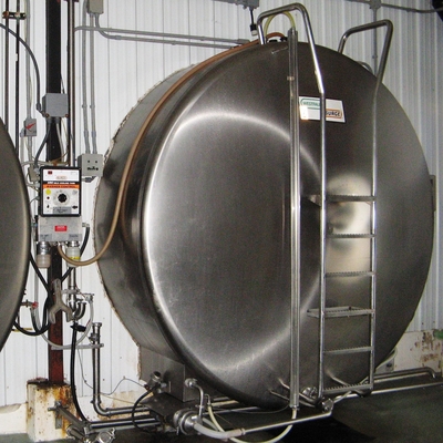 Large round stainless steel tank with ladder attached to pipes and other equipment