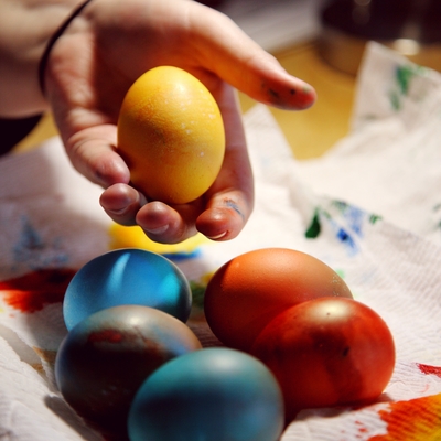A hand holding a yellow dyed eggs over multiple other dyed eggs.