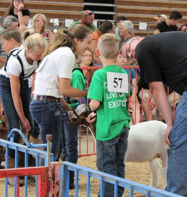 a 4-Her and a Cloverbud (younger) 4-Her are holding the leash of a goat and talking to a judge at the goat show