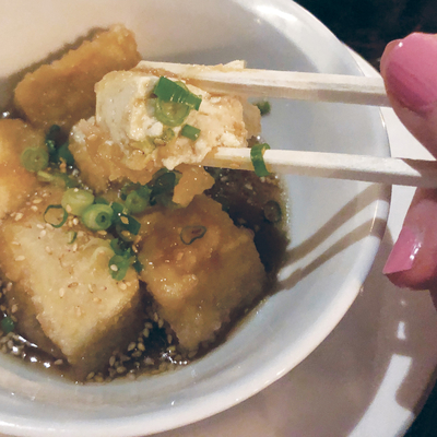 Chopstick reaching for a piece of fried tofu.