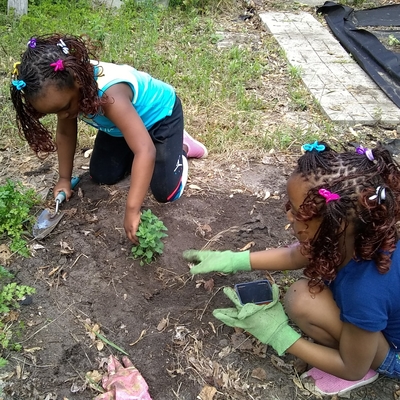 Two girls planting in a garden bed.