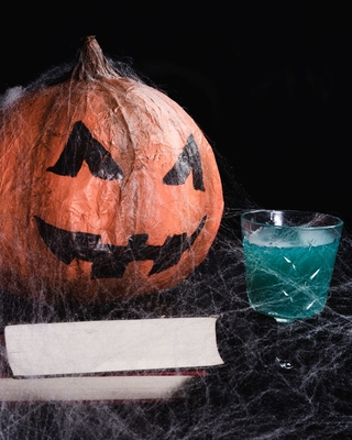 A jack-o-lantern next to a blue drink covered in spiderwebs.