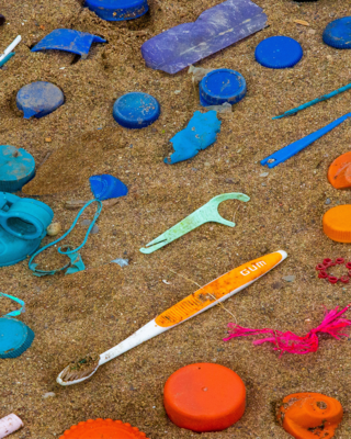 Plastic trash items arranged in rainbow order on sand. 