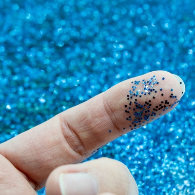 A close-up view of blue glitter on a finger, emphasizing the glitter's textured and shiny qualities.