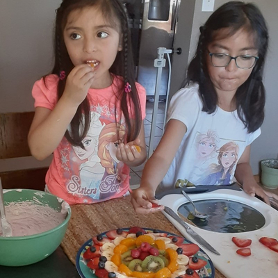 Two girls making fruit pizza at home.