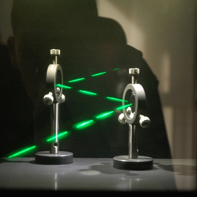 A green laser light going diagonally between two metal spheres on stands.