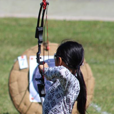 girl with dark hair shooting a bow and arrow at target