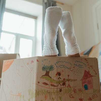 A cardboard box with two socked human feet coming out the top