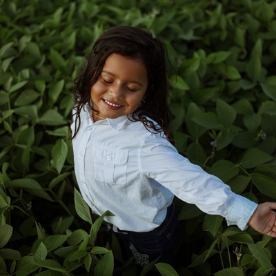 A girl smiling with her eyes closed standing in a field of green plants.