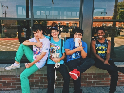 Four teen boys sitting together on a ledge of a building outside.