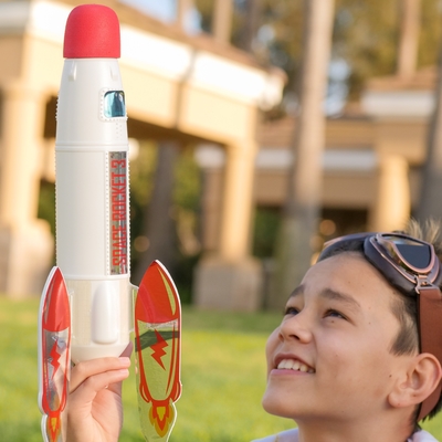 A boy wearing goggles on his head looking at a toy rocket 