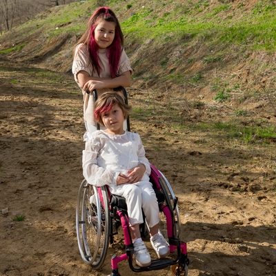 A girl standing behind a girl in a wheelchair