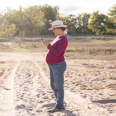 A pregnant woman on a hike checks her phone.