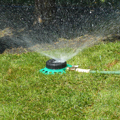 A green metal sprinkler watering an area of green grass.