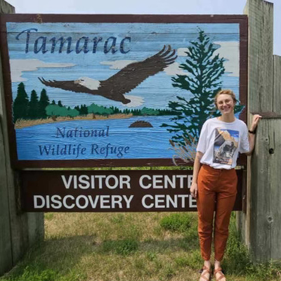 Myra McKee standing in front of the Tamarac Wildlife Refuge welcome sign