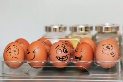 Brown eggs in clear container with faces of varying emotions drawn on them.