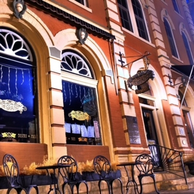 Nighttime front of the historic building with a lantern and patio tables in front. The windows are arched and have decorative metal work at the top.