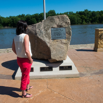 A tourist looking at a memorial dedicated to veterans near a river.