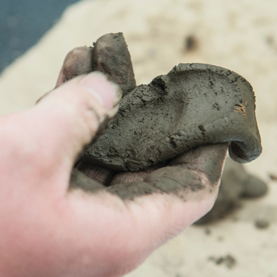 Hand holding a ball of wet soil that has been flattened into a ribbon.