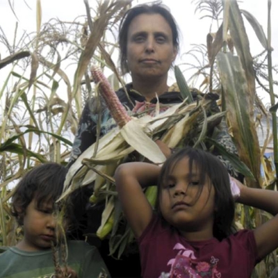 Woman holding a shucked cob or corn with two children in a corn field.