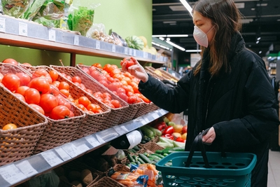 Woman selecting a tomato in a grocery store wearing a face mack.