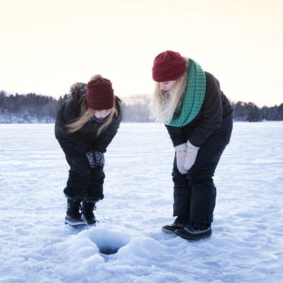 An woman and girl peer into an ice fishing hole on a frozen lake